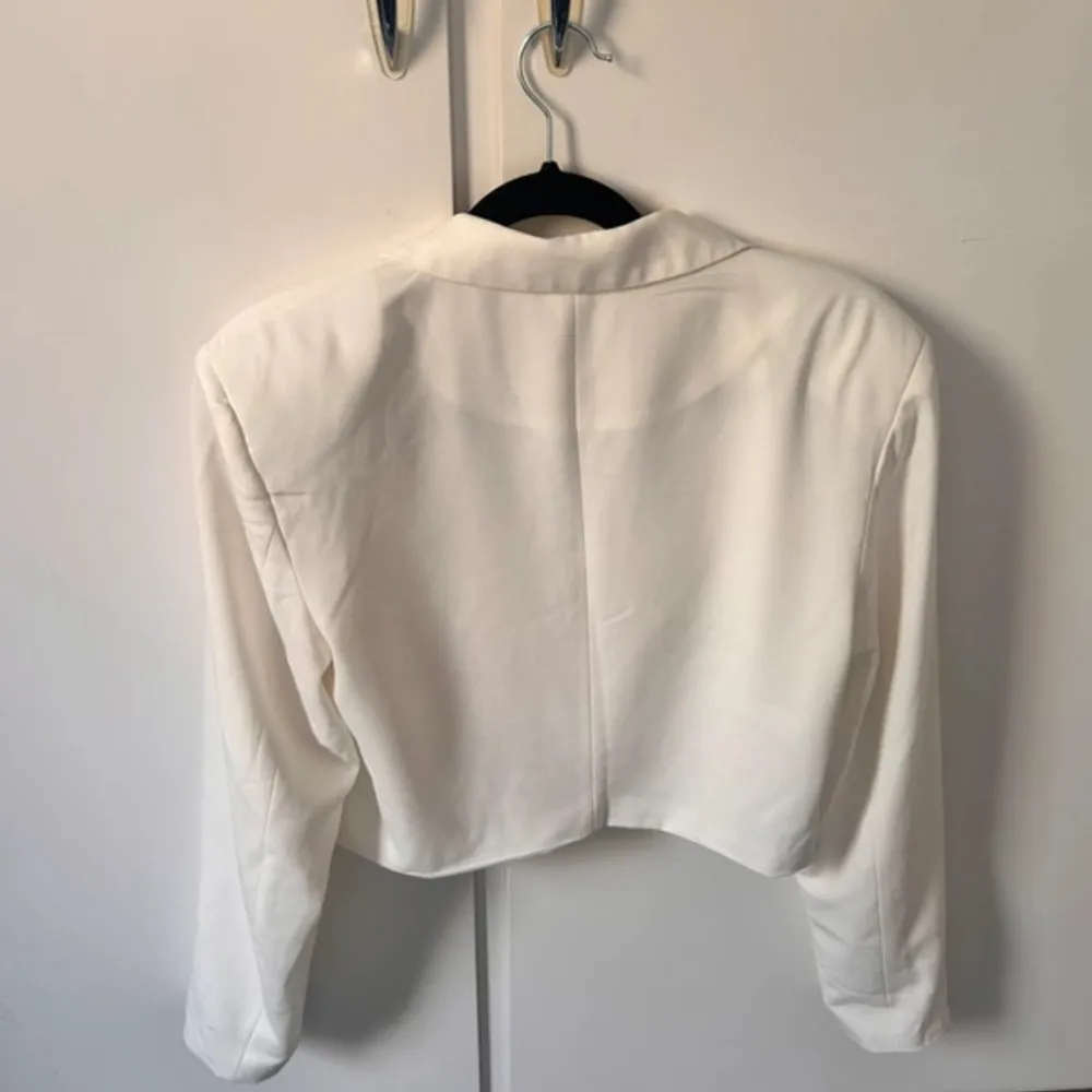 Säljer en stilren vit croppad kavaj från Nelly. Jackan har lång ärm, klassisk krage och knäppning framtill. Perfekt att styla med jeans eller kjol för en trendig look.. Puvut & Bleiserit.