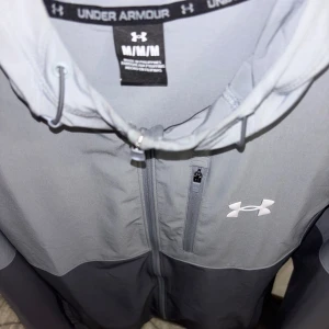 Grå vindjacka från Under Armour - Använt max 4 gånger, beställde fel storlek. Helt ny inga fel.