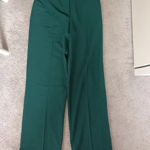 Mörkgröna kostymbyxor från BikBok - Snygga mörkgröna kostymbyxor från BikBok med raka ben och klassisk passform. Byxorna har hällor för bälte, diskreta bakfickor och stängs med dragkedja och knapp framtill. Super sköna och sitter snyggt men tyvärr försmå för mig. 90kr men det kan absolut diskuteras 