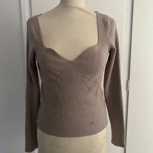 Beige ribbad tröja från SHEIN - Säljer en beige ribbad tröja från SHEIN med lång ärm och markerad byst. Tröjan har en fyrkantig ringning och är tillverkad i stretchigt material som sitter snyggt. Perfekt för dig som gillar stilrena basplagg.