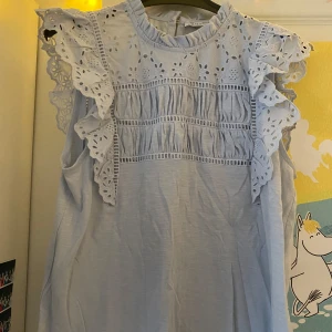 Ljusblå ärmlös blus med spets och volang - Supersöt ljusblå blus med broderade spetsdetaljer och volang vid axlarna. Blusen är ärmlös och har rund halsringning med fina hålbroderier framtill och baktill. Perfekt för sommaren ☀️😽🫶🏽