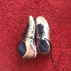 Guldiga Nike air fotbollsskor - Säljer ett par snygga fotbollsskor i guld. Skorna har snörning och en sportig design som passar perfekt för planen. Lätta och smidiga för snabba rörelser.