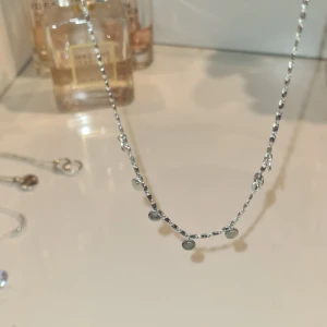 Silverfärgat halsband med små runda hängen - Säljer ett stilrent silverfärgat halsband med små, blanka runda hängen längs kedjan. Perfekt för att ge en enkel men elegant touch till din outfit. Passar bra att bära ensam eller att kombinera med andra smycken🩷