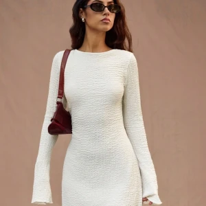 Vit klänning med öppen rygg - Snygg vit klänning med texturerat material och långärmad design. Den har en öppen rygg med knytband och är helt ny och oanvänd då den ej passade mig 💗