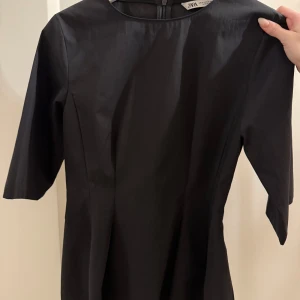 Svart blus - Säljer en stilren svart blus i storlek XS. Klänningen har rund halsringning, halvlånga ärmar och en figurnära passform. Perfekt för dig som gillar minimalistisk och elegant stil.