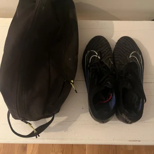 Svarta fotbollsskor med vita detaljer - Säljer ett par svarta fotbollsskor med vita mönster och snörning. Skorna har en sportig design och är perfekta för dig som gillar att spela fotboll. Snygga och funktionella med rund tå.