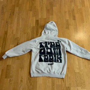 Vit hoodie från Pull&Bear STWD - Säljer en vit hoodie från Pull&Bear STWD med svart grafiskt tryck både fram och bak. Tröjan har huva med dragsko och en stor magficka. Perfekt för en avslappnad och cool stil.