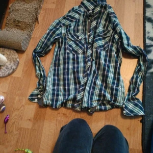 Blågrön rutig skjorta från Tailored Denim - Säljer en snygg rutig skjorta från Tailored Denim i blått, grönt och vitt. Skjortan har långa ärmar, knappar framtill och två bröstfickor. Perfekt för dig som gillar en avslappnad men stilren look.