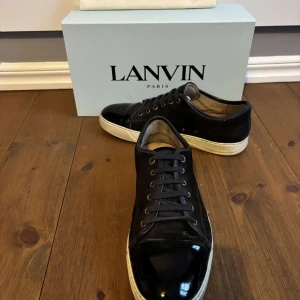 Navy sneakers från Lanvin - Vi säljer ett par lanvins i storlek 10/44. Dessa har använts i ett par månader men de har hålt sig i bra skick. Skorna bär små defekter vid sulan och kanten av skon. Skick 8/10. Nypris ligger på runt 5000 men säljer för 2349. Vid köp kommer Box, extra snören, kvitto, och ett clean kit. Hör av vid funderingar. Pris kan diskuteras!