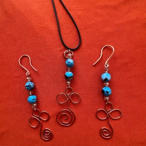 Handgjort smyckeset med blå pärlor och virad metall - Unikt set med örhängen och halsband. Smyckena har blå pärlor och dekorativa virade metalltrådar i spiralform. Halsbandet har svart snöre. Perfekt för dig som gillar boho-stil och färgglada detaljer.