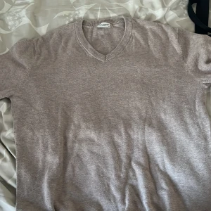 Beige v-ringad tröja från John Henric - Säljer en stilren beige v-ringad tröja från John Henric i 100% bomull. Tröjan har långa ärmar och ribbade muddar vid ärmslut och hals. Perfekt för lager-på-lager och passar till många olika outfits.