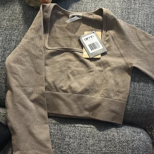 Beige croppad långärmad topp från Aim'n - Säljer en beige croppad långärmad topp från Aim'n med fyrkantig ringning. Toppen har en ribbad struktur och är perfekt för träning eller som ett snyggt basplagg. Alla 3 är oanvända tröjorna är i storlek s och bhn i xs
