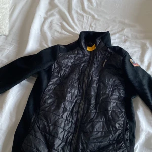 Parajumper jacka - Säljer en svart jacka från Parajumpers med quiltad front och slätare ärmar. Jackan har dragkedja och en patch på ena ärmen. Perfekt för kyligare dagar och har en sportig look. Köpt på kidsbrandstore för ca 2000 på rea egentligen 3000 mitt pris 700 storleken är y-m men passar ca 150-165, bra skick inga tydliga tecken på användning.