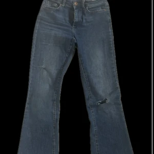 Blå bootcut jeansbyxor - Säljer ett par klassiska blå bootcut jeans med hög midja. Jeansen har fem fickor, knapp- och dragkedjestängning samt lätt slitna detaljer vid knäna. Perfekta för dig som gillar en tidlös denimlook med lite utsvängda ben.