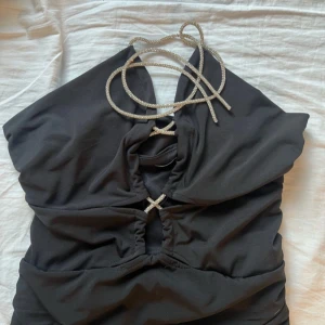 Svart topp  med glittriga detaljer - Snygg svart topp med glittriga snören och dekorativa korsdetaljer framtill. Perfekt för en stilren och elegant outfit .