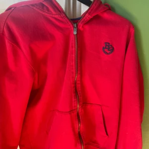 Röd huvtröja från Etirel - Säljer en jättesnygg röd huvtröja från Etirel med dragkedja och en liten logga på bröstet. Tröjan har långa ärmar och en praktisk huva.