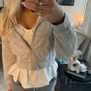 Grå croppad hoodie - Säljer en stilren grå croppad hoodie med dragkedja framtill. Perfekt för en avslappnad look. Den har långa ärmar och en bekväm passform.