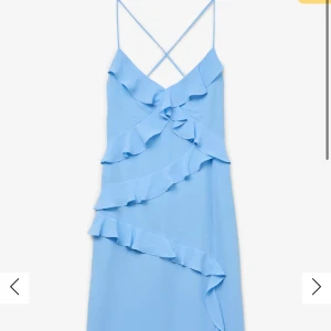 Ljusblå klänning med volanger från Vero Moda - Snygg ljusblå klänning med volanger och smala axelband. Klänningen har en öppen rygg med korsade band och en elegant slits framtill. Perfekt för sommarens fester! Helt ny prislapp kvar , nypris 800kr