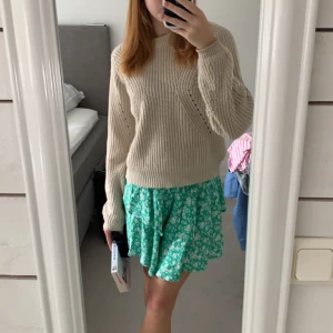 Grön blommig volangkjol - Säljer en söt grön kortkjol med vitt blommönster och volangdetaljer. Kjolen har smock i midjan för extra komfort och en luftig känsla. Perfekt för varma dagar och enkel att styla med en stickad tröja eller topp. 