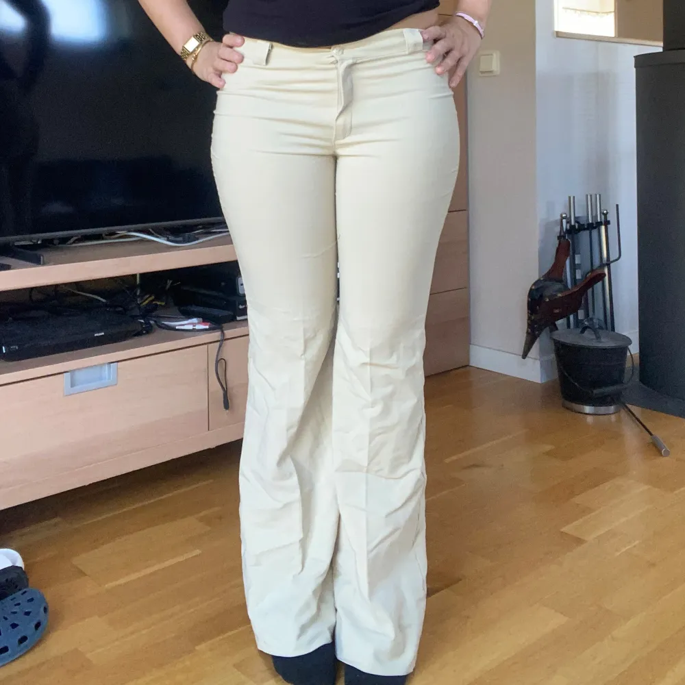 Snygga beige kostymbyxor med bootcut passform och lågmidja . Byxorna har klassisk dragkedja och knapp framtill samt pressveck längs benen. Perfekta för en stilren och trendig look. Står ingen storlek men passar mig som har S . Farkut & Housut.