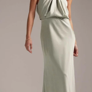 Ljusgrön långklänning - Elegant ljusgrön långklänning med en draperad design och halterneck. Perfekt för en stilfull kväll. Klänningen har en mjuk och flytande passform som ger en vacker siluett.