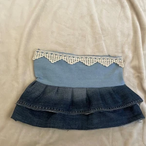 Jeanskjol med spetsdetalj - Charmig jeanskjol i två nyanser av blått med volanger och en vacker spetskant upptill. Kjolen har jag skälv sytt🩷midjemått: 74 cm totalt och längd: 30cm