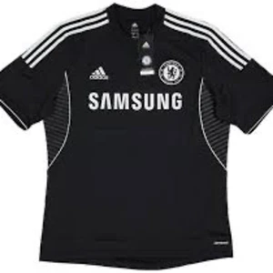 Svart Chelsea fotbollströja från Adidas - Säljer en svart Chelsea fotbollströja från Adidas med korta ärmar. Tröjan har vita detaljer och texten 'Samsung' på framsidan. På baksidan finns namnet 'Hazard' och nummer 10!