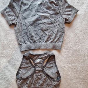 Workout Empire - Grått träningsset med geometriskt mönster - Snyggt grått träningssetmed geometriskt mönster, använd bara några gånger. Kortärmad topp,  cropp top och matchande leggings. Setet har ett geometriskt mönster och är tillverkat i ett mjukt och stretchigt material.