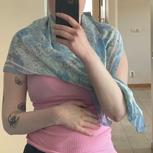 Blommig ljusblå och vit sjal - Säljer en tunn och luftig sjal med blommigt mönster i ljusblått, vitt och inslag. Perfekt accessoar för att liva upp din outfit. Halsduken är rektangulär och känns mjuk mot huden.