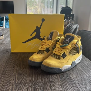 Nike Air Jordan 4 Retro 'Lightning' sneakers - Säljer ett par Nike Air Jordan 4 Retro 'Lightning' sneakers i gul mocka med grå och svarta detaljer. Skorna har klassisk snörning, meshpaneler och vit sula. Perfekta för dig som vill sticka ut med en ikonisk och färgstark sneaker.