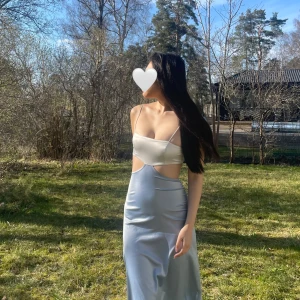 ASOS Design satinklänning - Elegant klänning med vit topp och ljusblå kjol från ASOS Design. Axelbandslös design med cut-out detaljer i midjan. Perfekt för sommarens festligheter. Nyskick, prislappen ligger fortfarande kvar.