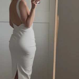 Vit långklänning med öppen rygg från Zara - Säljer en vit långklänning från Zara med djup öppen rygg. Klänningen har en figurnära passform och slits bak. Perfekt för sommaren. Den har en liten defekt som visas på bild men absolut inget man tänker på! Hör av er vid intresse:)