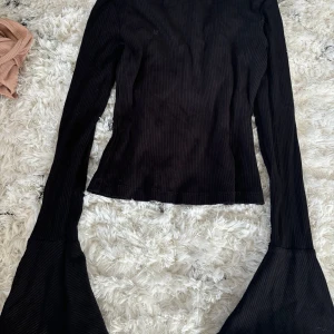  ribbad topp med trumpetärmar  NA-KD - Säljer en stilren svart ribbad tröja från NA-KD. Tröjan har långa ärmar med vida ärmslut som ger en trendig look. Perfekt för att uppgradera garderoben med en modern touch. Utan anmärkningar.
