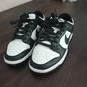 Nike Dunk strl 40 - Säljer ett par stilrena Nike Dunk sneakers i svart och vitt. Skorna har en klassisk design med snörning och Nike-logga på sidan och hälen. Perfekta för en sportig look.