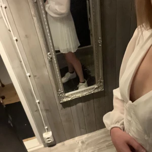 Studentklänning  - Elegant vit klänning med v-ringad design och långa ärmar. Klänningen har ett plisserat kjolparti och en smickrande passform i midjan. Perfekt för speciella tillfällen. Köpte denna till studenten, men är blir inte denna och går tyvärr inte att skicka tillbaka den.. så prislapp sitter kvar, bara testad! Jag är 170 lång, köpt från bubbleroom!! Strl 34/Xs