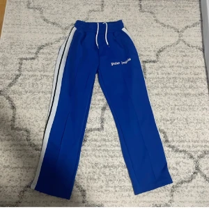 Blå mjukisbyxor från Palm Angels - Snygga blå mjukisbyxor från Palm Angels med vita sidoremsor och snörning i midjan. Perfekta för en avslappnad stil med en touch av sportig elegans.