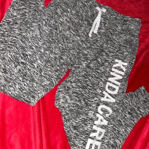 Gråmelerade mjukisbyxor med tryck - Säljer ett par gråmelerade mjukisbyxor med vit text 'KINDA CARE, kinda don’t' längs ena benet. Byxorna har snörning i midjan och är gjorda i mjukt material, perfekta för chill dagar. Snygg och avslappnad stil. 