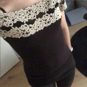 Spets body från intimissmi - Supersnygg svart offshoulder topp från intimissmi med ljus spetsdetalj i blommönster över byst och ärmar. Tight passform och korta ärmar som sitter precis på axlarna. Perfekt för dig som vill sticka ut med en romantisk och trendig look. Går ej att få tag på i butik