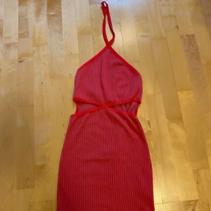 Röd omlottklänning från Zara S - Säljer en röd kortklänning från Zara i storlek S. Klänningen har smala axelband som korsas i nacken, omlottdetalj framtill och ärmlös design. Materialet är mjukt och har ett diskret randigt mönster. Perfekt för dig som gillar trendiga och färgstarka plagg.