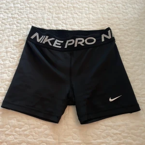Nike Pro svarta träningsshorts - Nike Pro svarta träningsshorts med bred elastisk midja och stor logga. Dri-FIT material som andas och håller dig torr under träningen. Tight passform och klassisk Nike Swoosh i vitt på benet. Perfekta för gymmet eller sport.