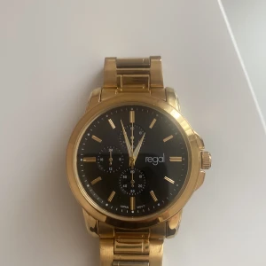 Guldig klocka från Regal med svart urtavla - En fin guld klocka som är råstfritståll från regal