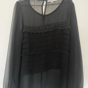Svart blus med volang och spetsdetaljer - Säljer en såååå fin svart blus! Jag säljer eftersom jag rensar ut min garderob och tyvärr får det inte plats mer. Blusen har jättefina broderade detaljer och ärmarna är see-through. Den är helt ok använd men i jättefint skick! Märket är Flashwoman, lite vintage. Storlek M