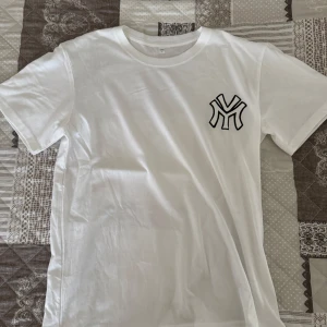 Vit t-shirt New York Yankees - Snygg vit t-shirt från Roy Srouf med stort tryck på ryggen och mindre loga på framsidan. Trycket har coola egyptiska detaljer och texten 'ATLANTIS'. Är en L men sitter som en S