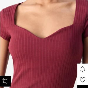 Vinröd ribbad topp med sweetheart-ringning - Snygg vinröd topp med ribbad struktur och korta ärmar. Toppen har en hjärtformad-ringning. Figurnära passform som framhäver siluetten, perfekt att styla med jeans eller kjol.