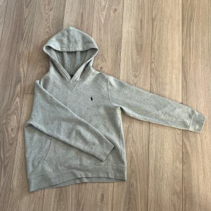 Grå hoodie från Polo Ralph Lauren - Säljer en grå hoodie från Polo Ralph Lauren med klassisk huva och känguruficka. Tröjan har lång ärm och en liten mörkblå häst på bröstet. Riktigt snygg tröja och skön! Säljer pga att den är för liten🥲det är storlek L i barn men sitter som en xs/xxs. skriv gärna om ni har någon fundering. Pris kan diskuteras!                                            Nypris: 1195