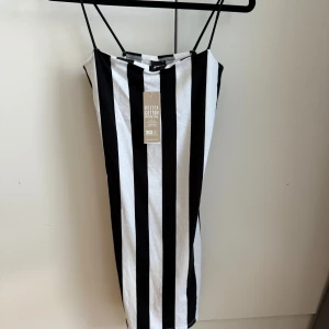 Randig kortklänning från Gina Tricot - Snygg kortklänning från Gina Tricot med breda svarta och vita ränder. Klänningen har smala axelband och är figurnära i modellen. Tillverkad i mjuk bomull, perfekt för dig som gillar en enkel men cool look.