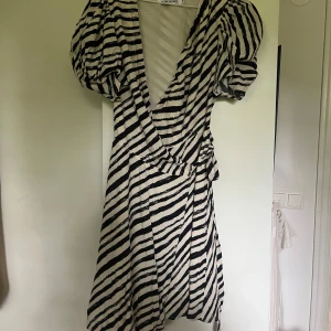 Zebramönstrad omlottklänning Adoore - Supersnygg kort omlottklänning från Adoore med zebramönster i svart och vitt. Klänningen har puffiga korta ärmar, markerad midja med knyt och djup v-ringning. 