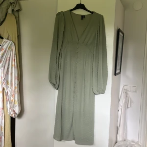 Ljusgrön långklänning från Vero Moda - Supersöt ljusgrön långklänning från Vero Moda med v-ringning, långa puffärmar och knappar framtill.  