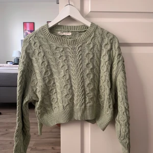 Grön kabelstickad tröja från Pull&Bear - Snygg ljusgrön kabelstickad tröja från Pull&Bear med croppad passform. Tröjan har rund halsringning, långa ärmar och breda ribbade muddar. Perfekt för lager-på-lager och chill vibes.