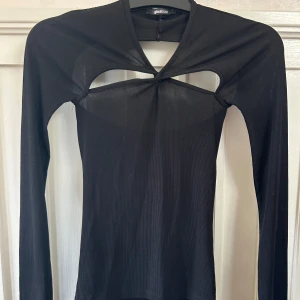 Svart ribbad topp med cut out Gina Tricot - Svart långärmad topp från Gina Tricot i ribbad stretchig polyester. Snygg cut out-detalj framtill som ger en cool look. Figurnära passform och rund halsringning. Perfekt för dig som vill sticka ut lite extra.